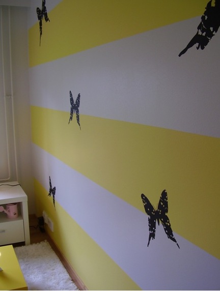 Erinevate värvitoonidega kujundatud seina aluspind, millele on šablooniga peale maalitud liblikamotiivid.
